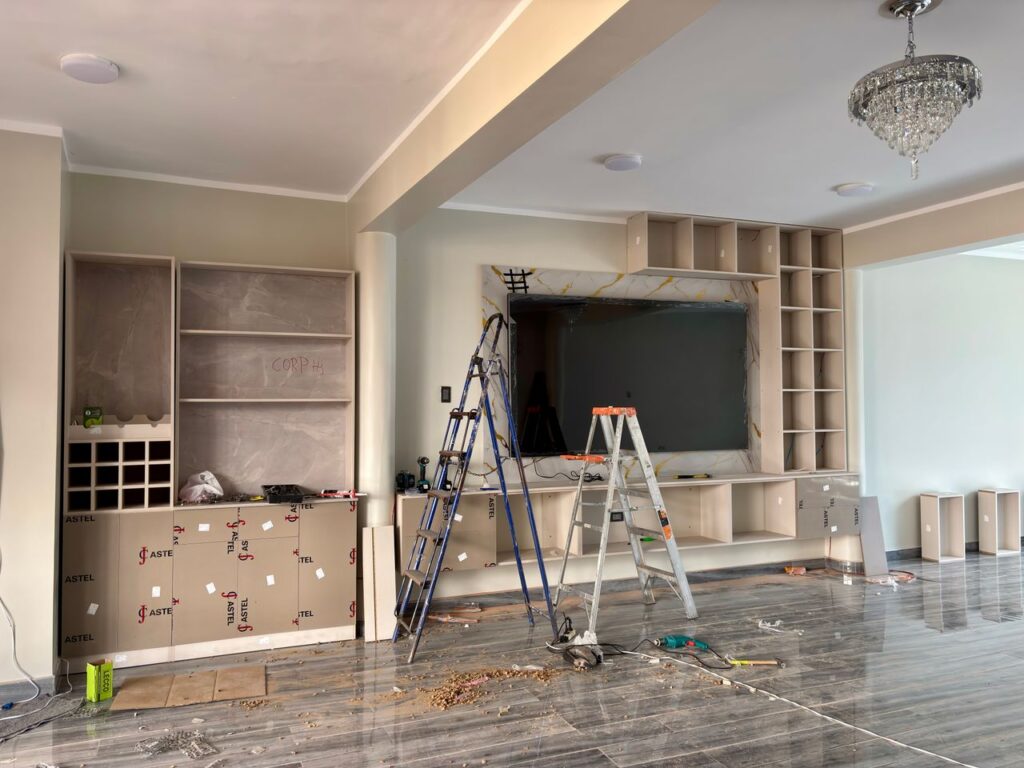 Living room renovation with built-in shelving under construction, two ladders, and tools on the floor.