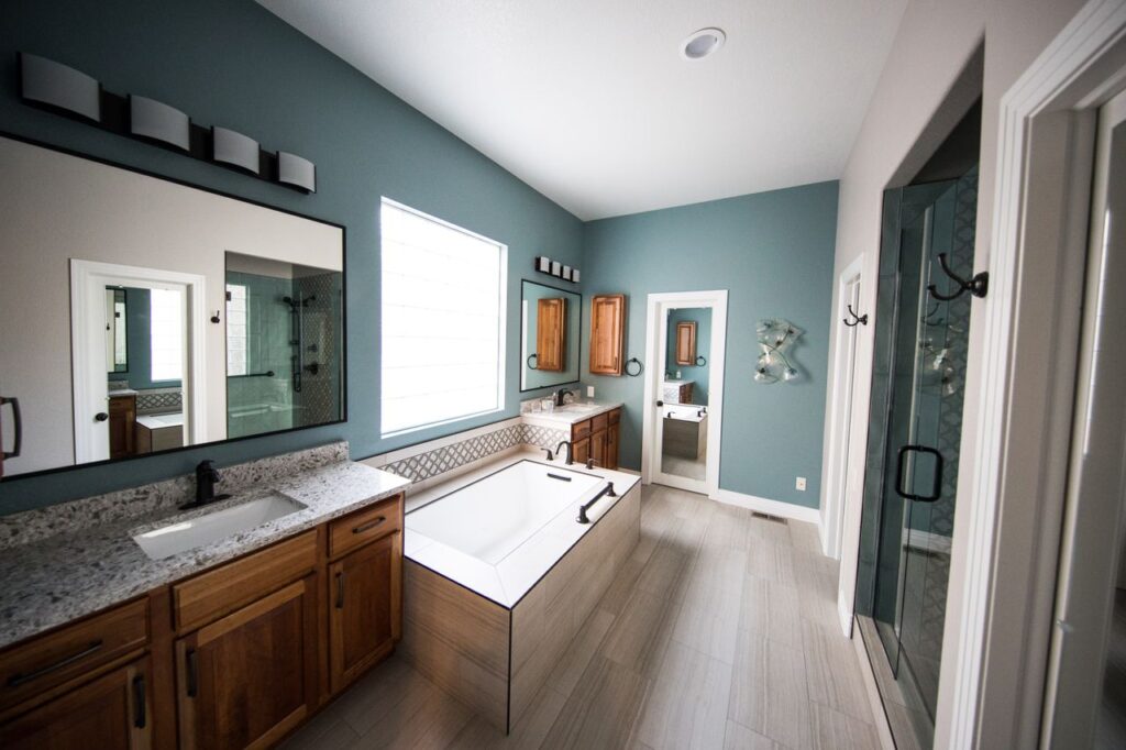Whole home makeover inspiration featuring a bathroom with teal walls, wood vanities, a soaking tub, and a glass shower.