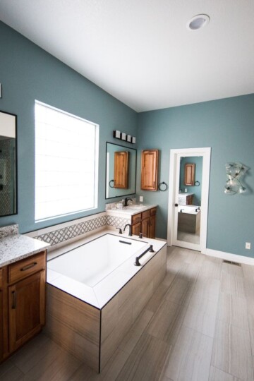 Whole home makeover inspiration featuring a bathroom with teal walls, wood vanities, a soaking tub, and a glass shower.
