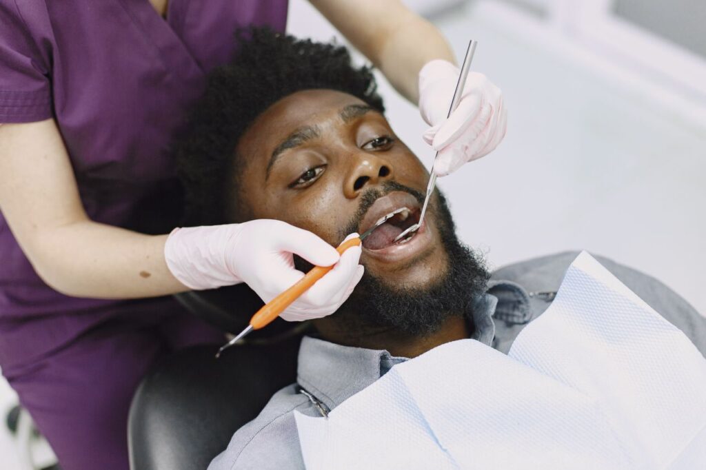 Dentist examining a patient&rsquo;s teeth with a dental mirror and handheld instrument.
